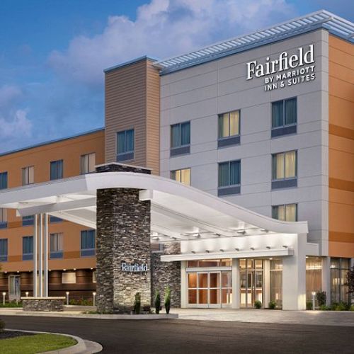 The image shows a Fairfield by Marriott hotel exterior with a modern design, featuring an illuminated entrance and multiple stories.