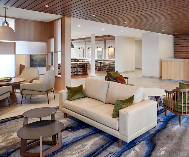 A modern hotel lobby with sitting area, couches, chairs, tables, art on the wall, and a reception desk in the background.