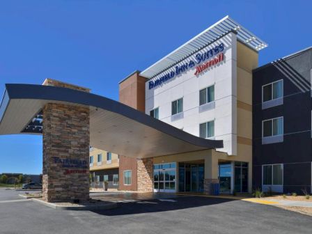 The image shows the entrance of a Fairfield Inn & Suites by Marriott hotel. There is a canopy over the entrance and a clear sky in the background.