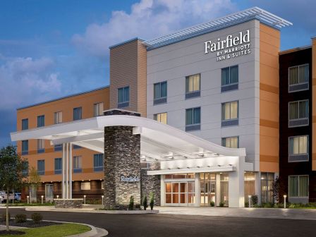 The image shows the exterior of a Fairfield by Marriott Inn & Suites hotel with a modern design, illuminated entrance, and well-maintained landscaping.