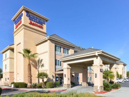 A beige, multi-story hotel building with signage, palm trees, and a covered entrance is shown under a clear blue sky.