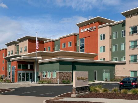 This image shows the exterior of a Residence Inn hotel, complete with modern architecture, an American flag, and a parking area.